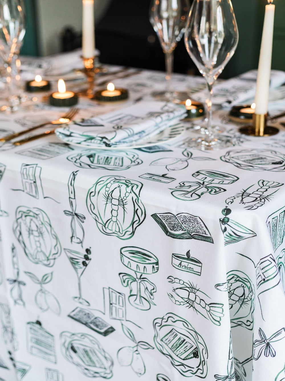 Table setting with a decorative tablecloth featuring green illustrations on a white background.