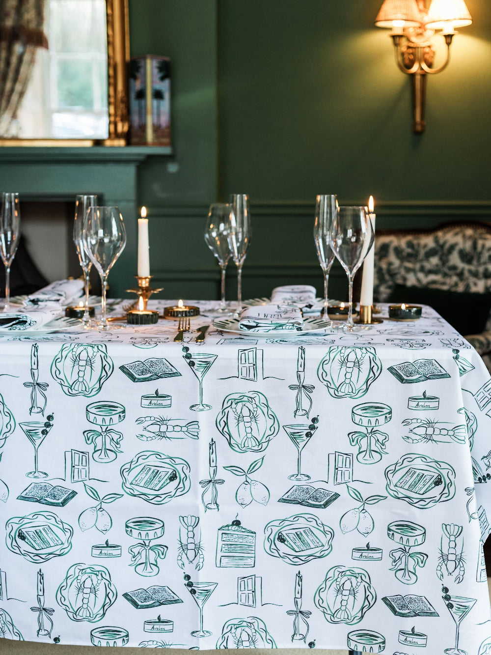 Dining table set with a decorative tablecloth featuring illustrations, candles, and wine glasses.