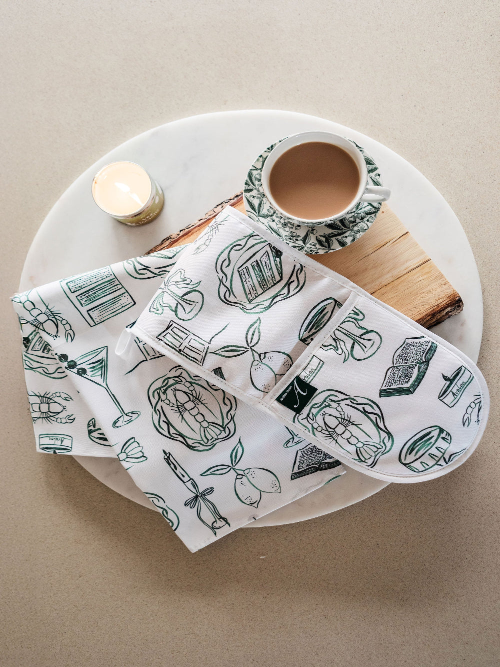 Set of illustrated tea towels with green and white designs on a wooden board.