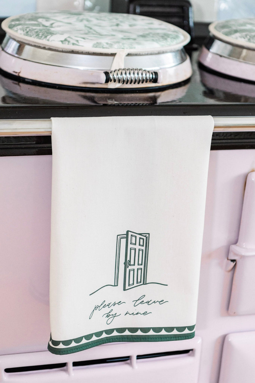 Kitchen tea towel with 'please leave by 9' hanging on a stove.