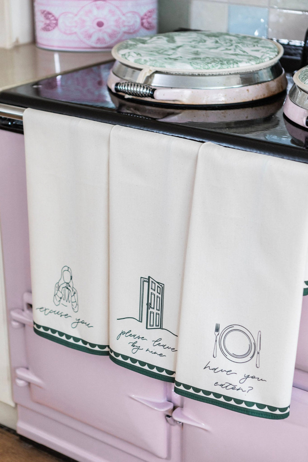 Three kitchen towels with printed designs hanging on a stove.