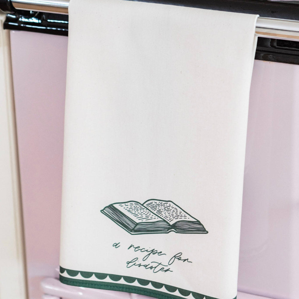 Kitchen towel with a green design and 'a recipe for disaster' text hanging on a rack.