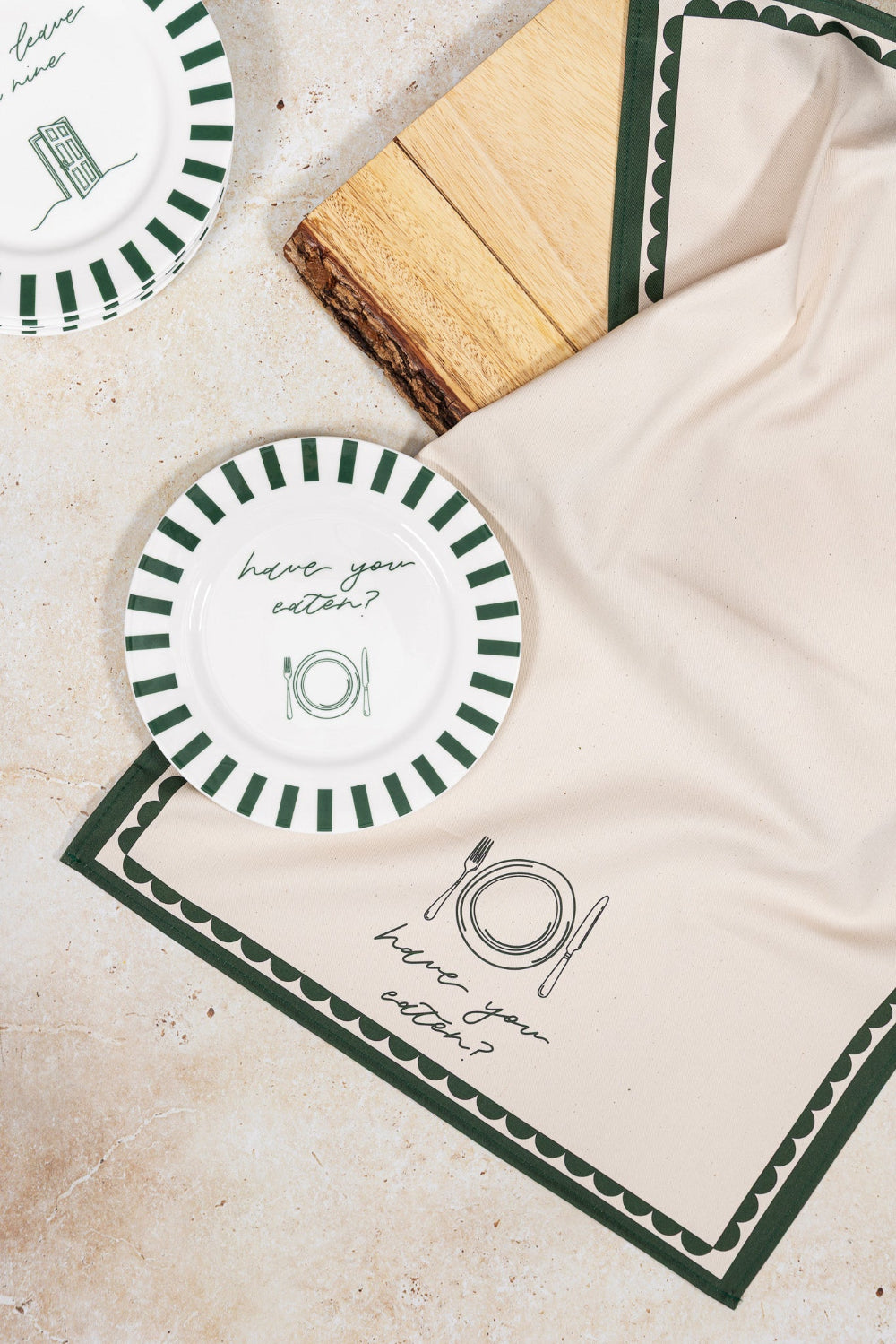 Round plates with green stripes and 'have you eaten' text and border on a beige matching teatowel