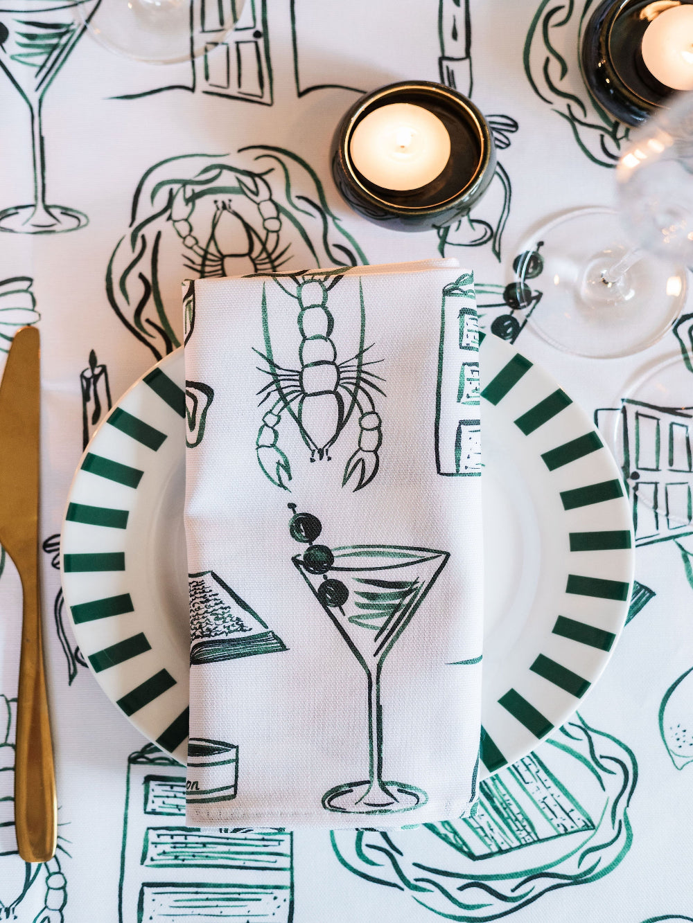Table setting with striped plates, cocktail napkin, and candle on a patterned tablecloth.