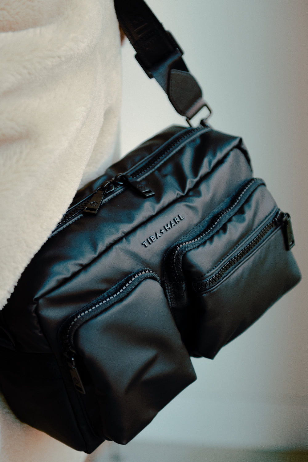 Black waist bag with visible brand name 'Tiba + Marl' on a blurred background