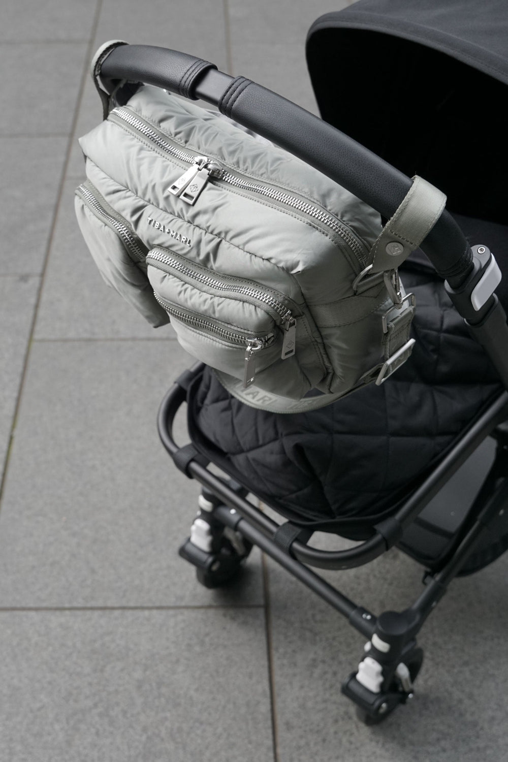 Sage Green buggy bag carrier with zipped pockets attached to pram outside