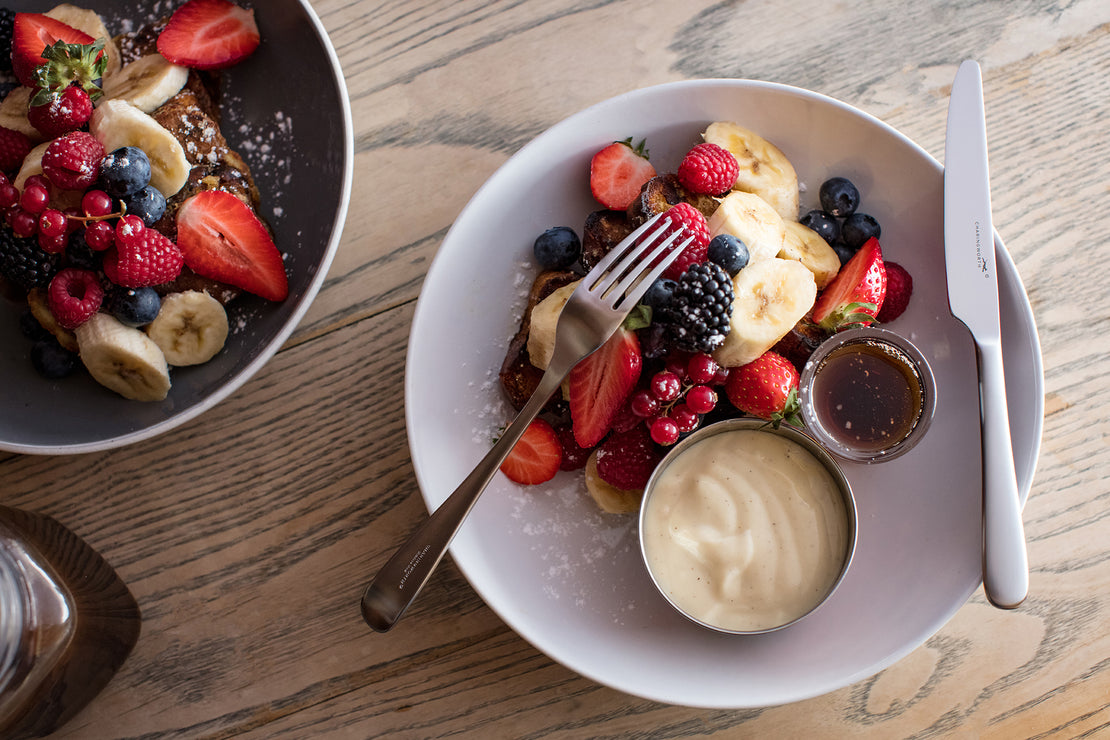 Two plates of fruit salad with waffles on a wooden table.