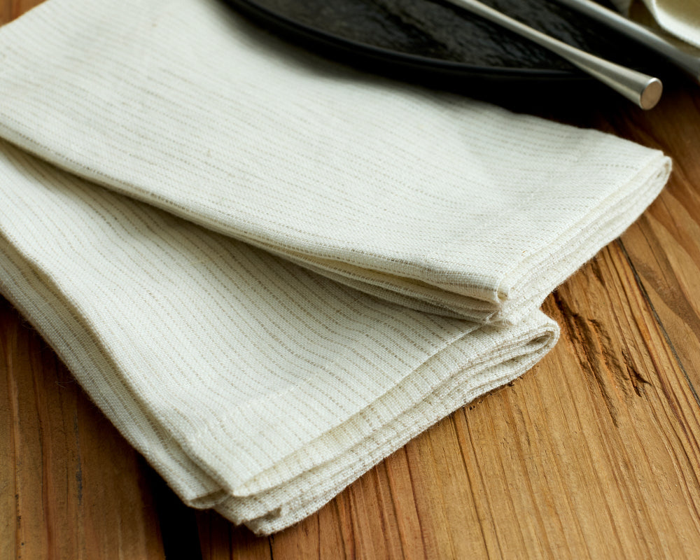 Folded white napkin on a wooden surface with a dark plate and silverware.