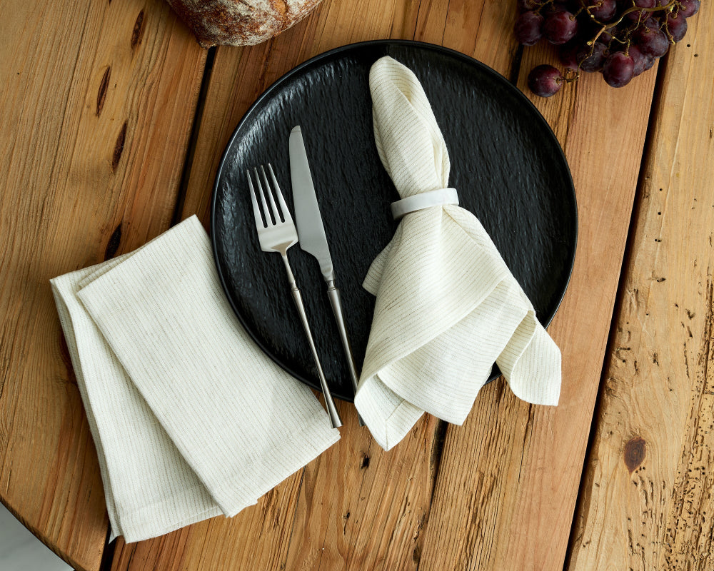 Black plate with white napkin, fork, and knife on a wooden table.