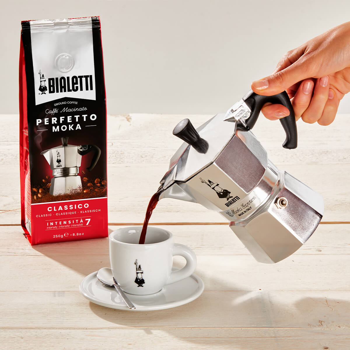 Bialetti Moka pot pouring coffee into a cup with a Bialetti coffee bag in the background.