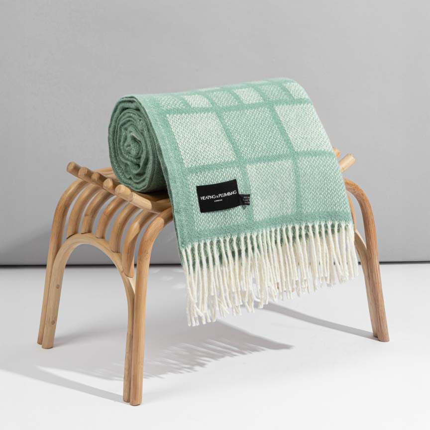 Green checkered blanket with white fringe draped over a wooden stool on a gray background