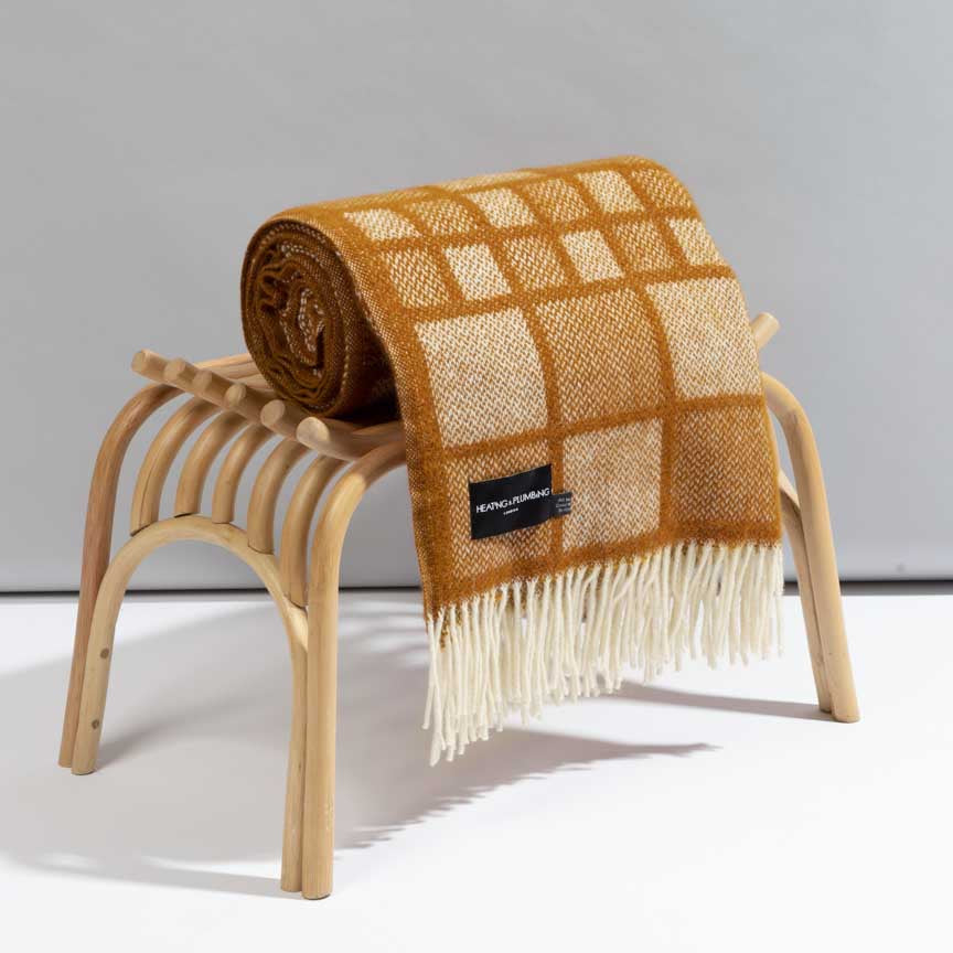 Plaid blanket with fringes draped over a wooden stool on a light grey background