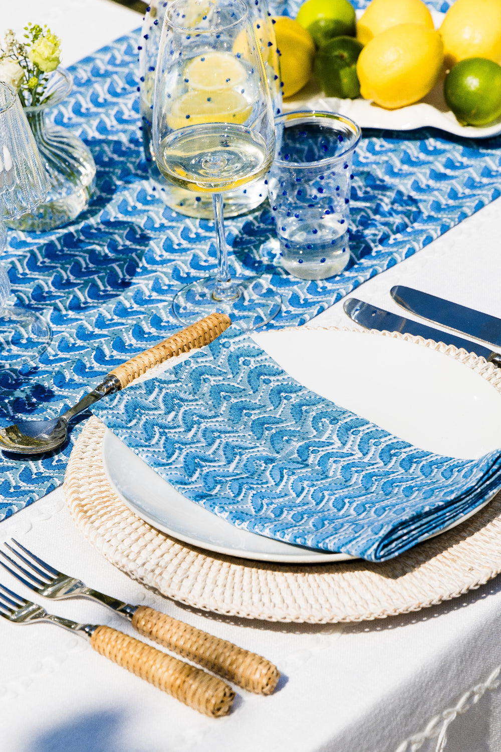 Table setting with blue patterned tablecloth, white plates, and cutlery on a white table.