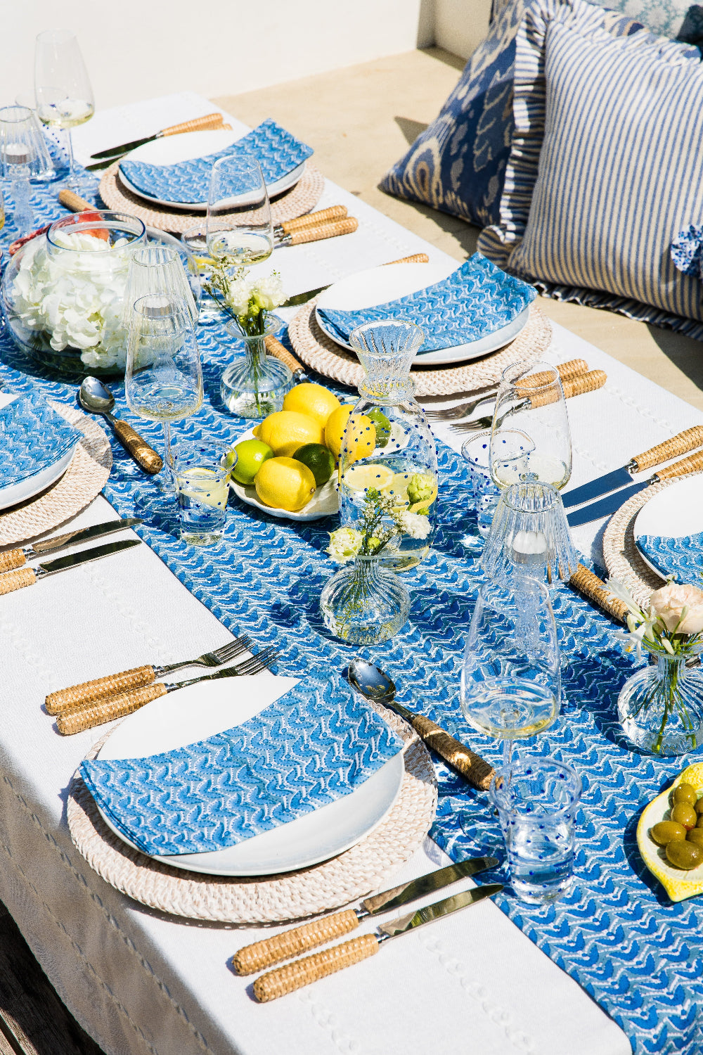 Outdoor table setting with blue and white tablecloth, plates, glasses, and decorative items.