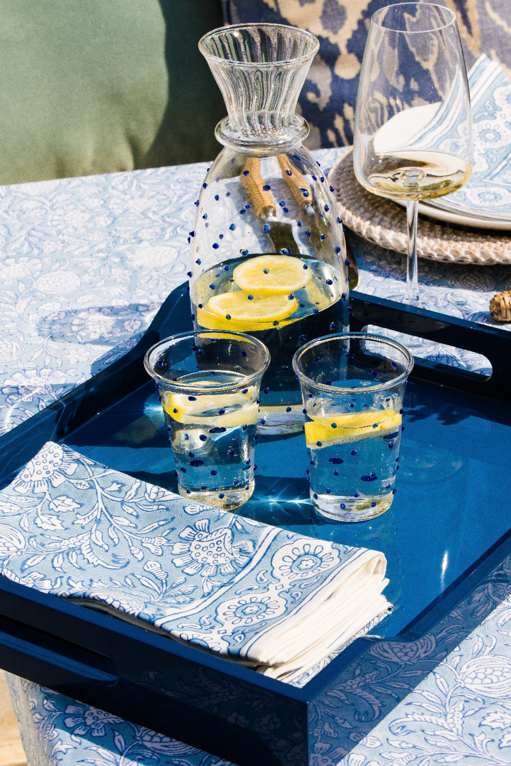 Tray with glasses of lemon water and a pitcher on a table with a blue and white patterned cloth.