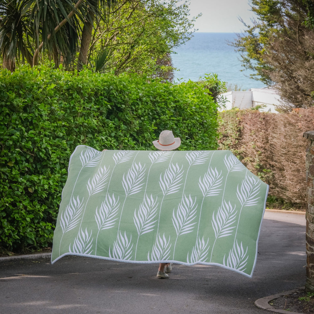 Green towel with white leaf pattern on a path with greenery and ocean view