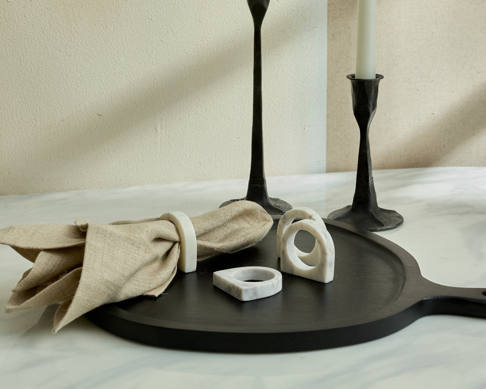 Decorative items including a black tray, beige napkin, polished marble napkin rings and candle holders on a neutral background