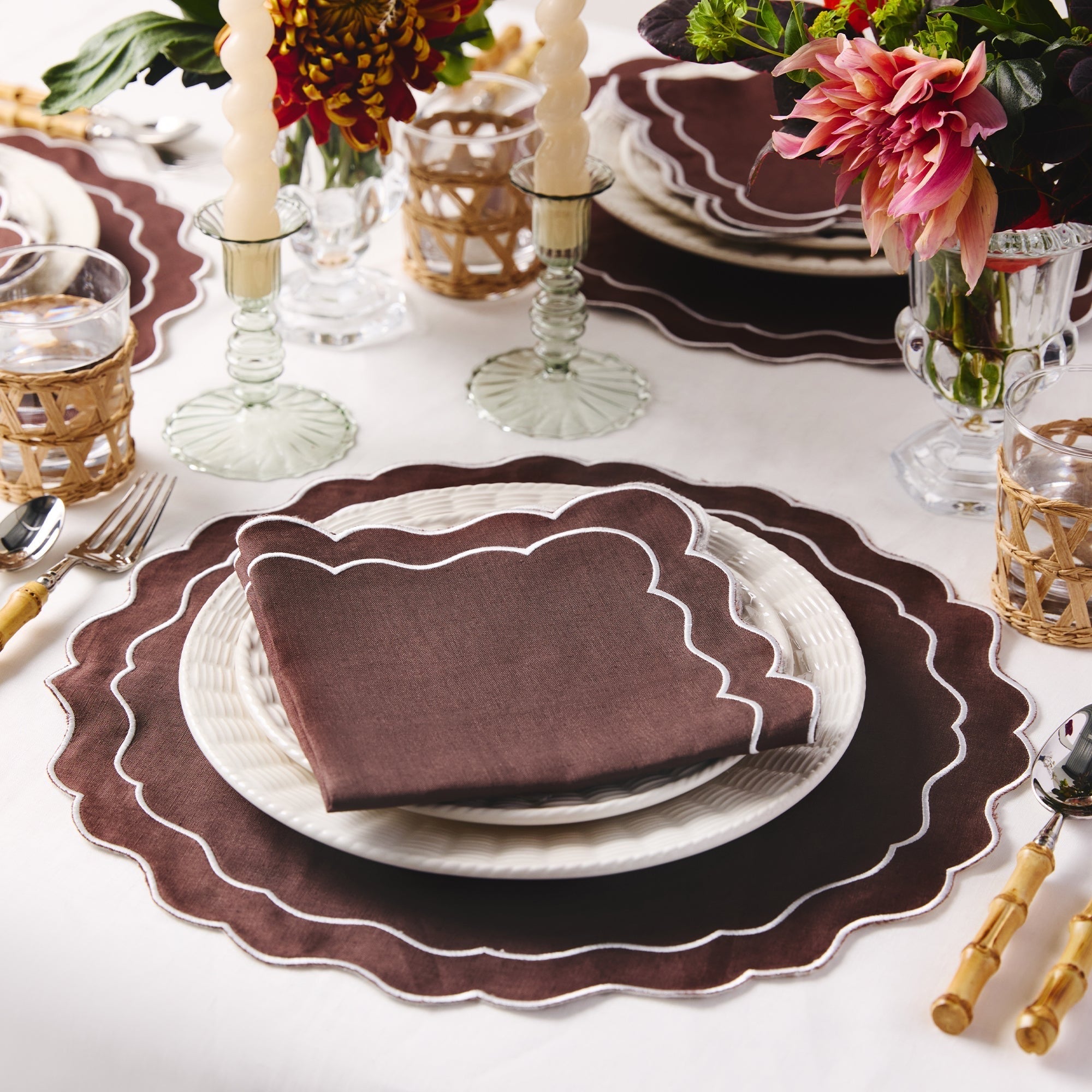 Elegant table setting with brown placemats, white plates, and gold cutlery on a white tablecloth.