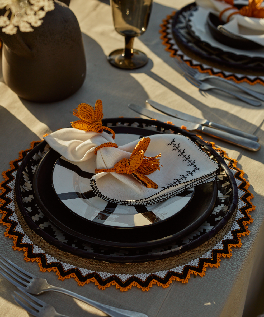 Decorative table setting with black plates, white napkins, and orange accents on a light-colored tablecloth.