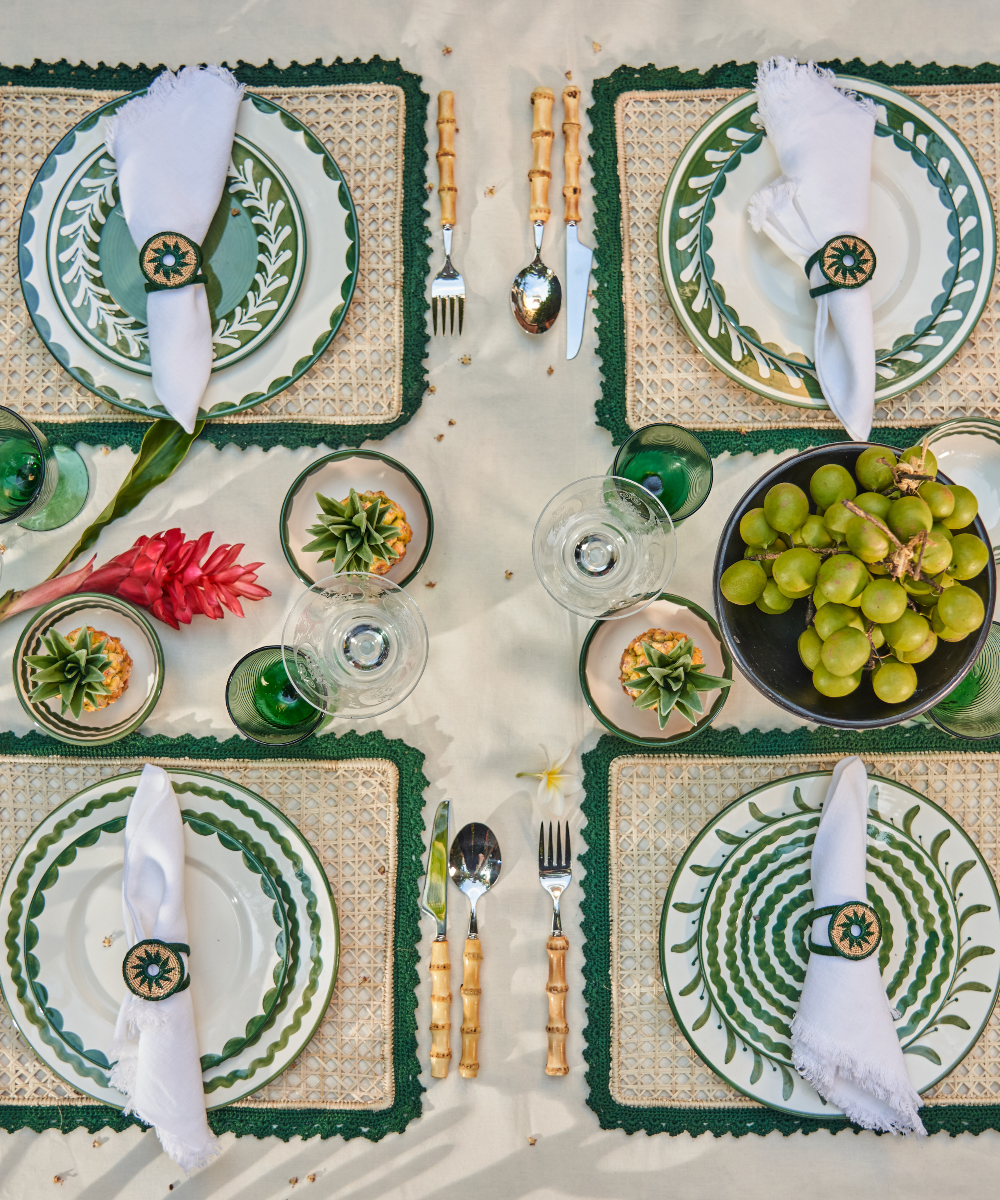 Elegant table setting with green and white plates, cutlery, and decorative elements on a textured surface.