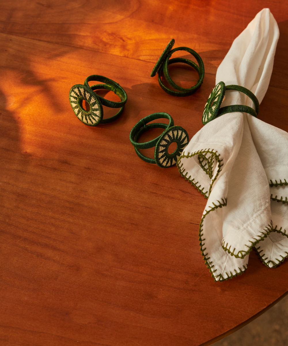 Green decorative napkin rings on a wooden surface with a white embroidered napkin.