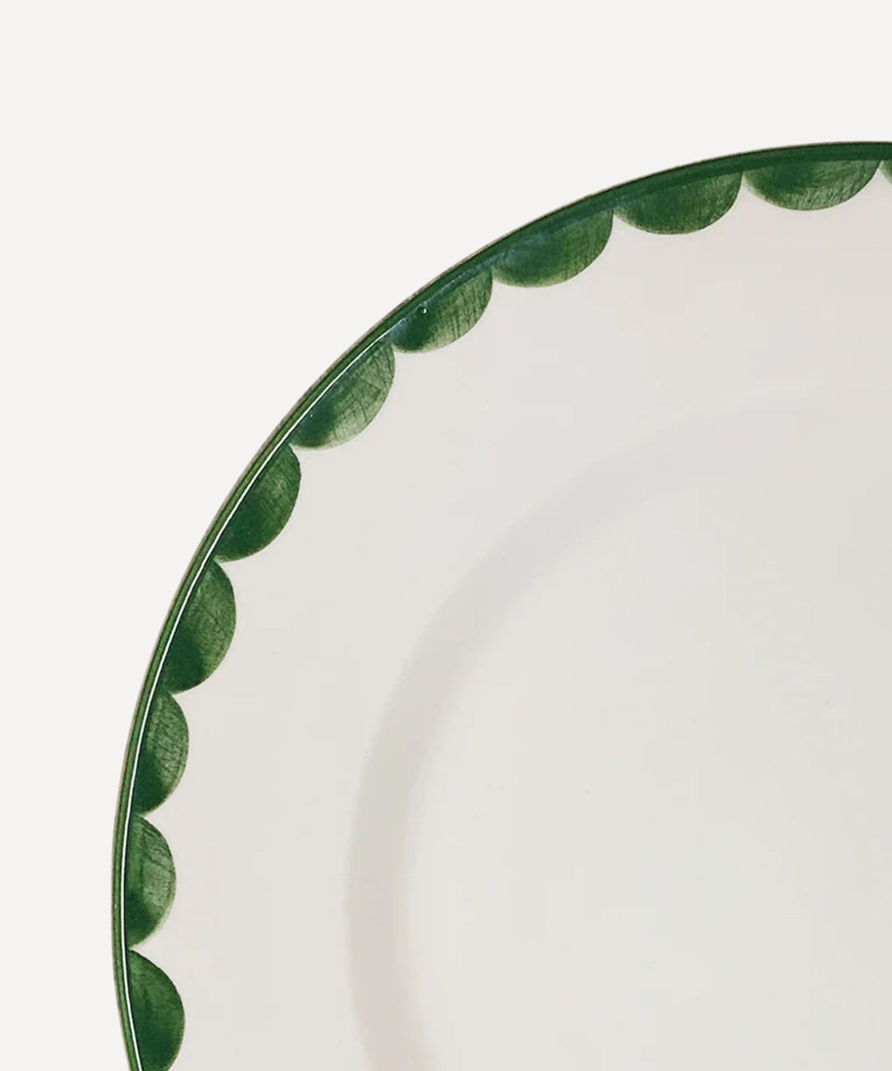Cloesup of a white ceramic dinner plate with fern green scalloped design on a white background