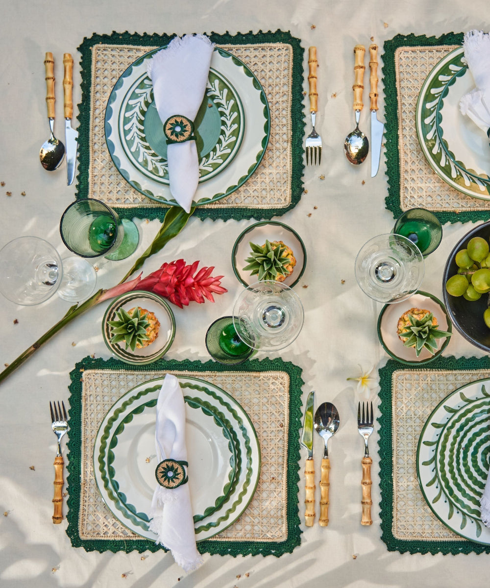 Elegant table setting with green and white plates, cutlery, and decorative elements on a neutral background.