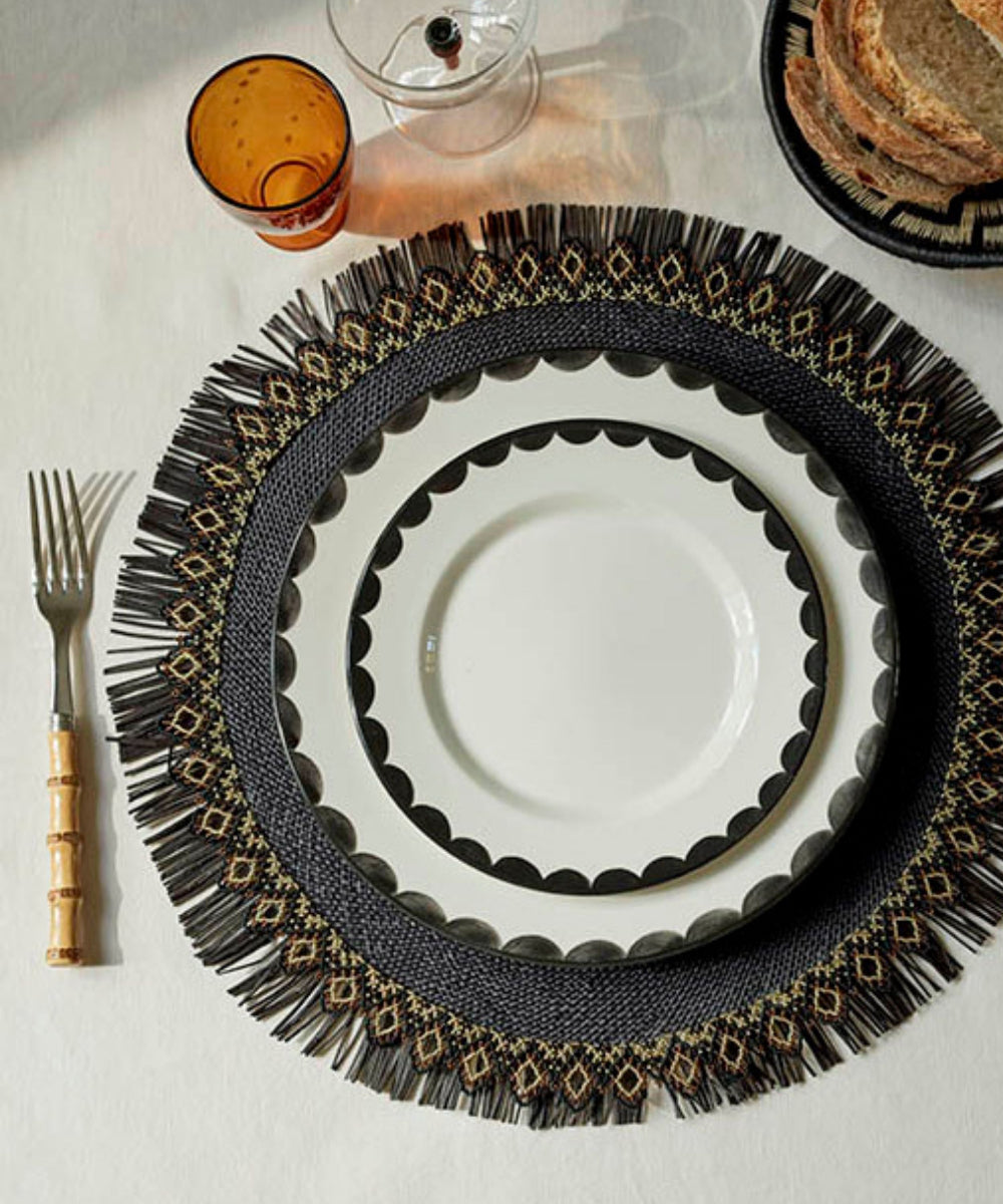 Decorative table setting with a black and gold placemat, white plate, and cutlery on a light surface.