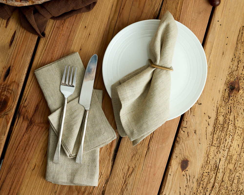 White plate with folded beige napkin, fork, and knife on a wooden surface