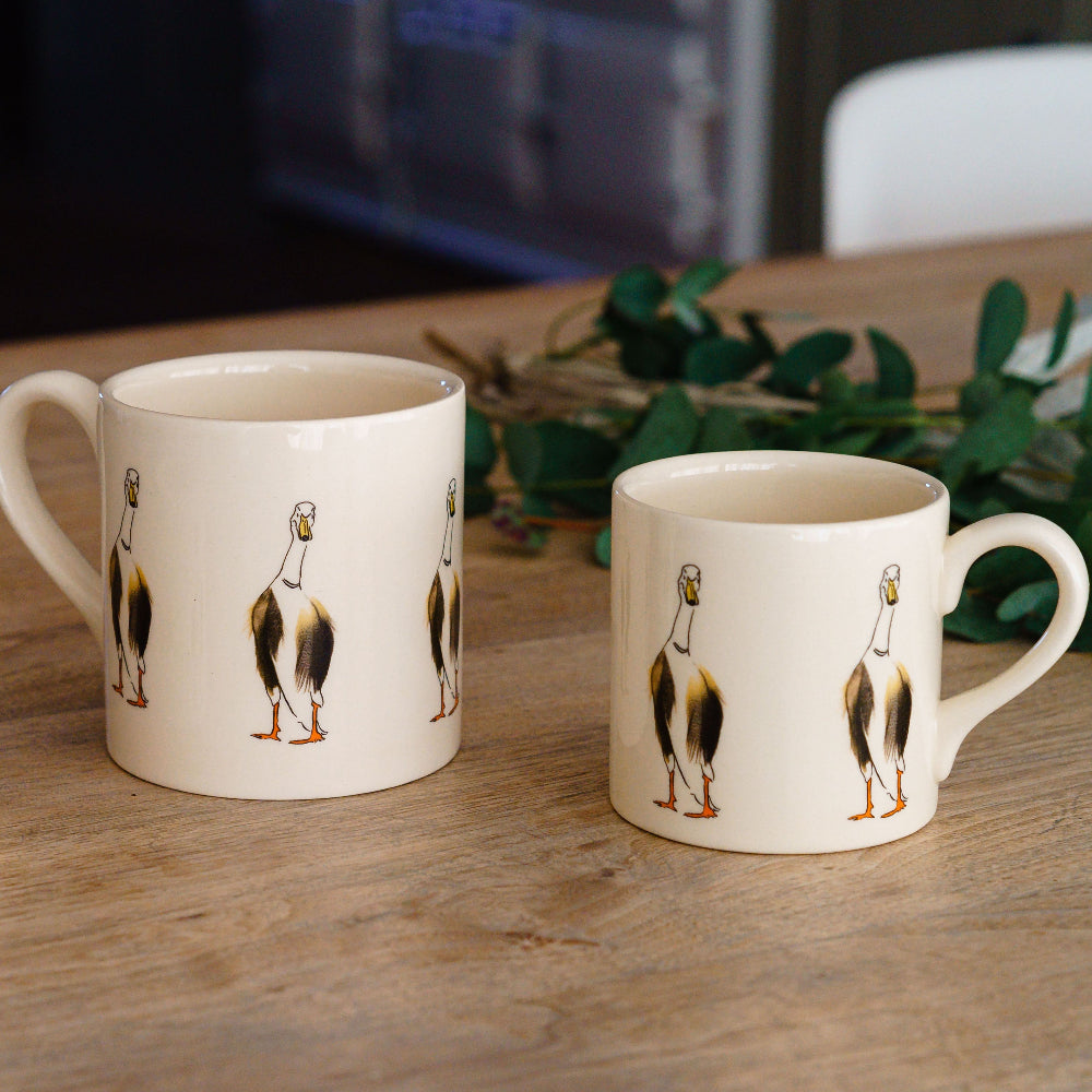 Two ceramic mugs with duck illustrations on a wooden surface.