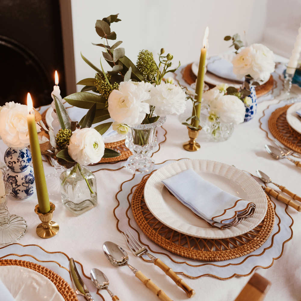 Elegant table setting with white flowers, candles, and gold accents on a white tablecloth.