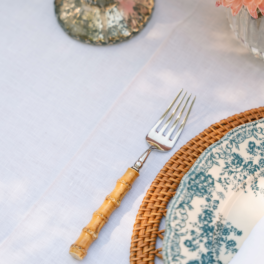 Silver fork with a bamboo handle on a woven placemat with a floral plate.