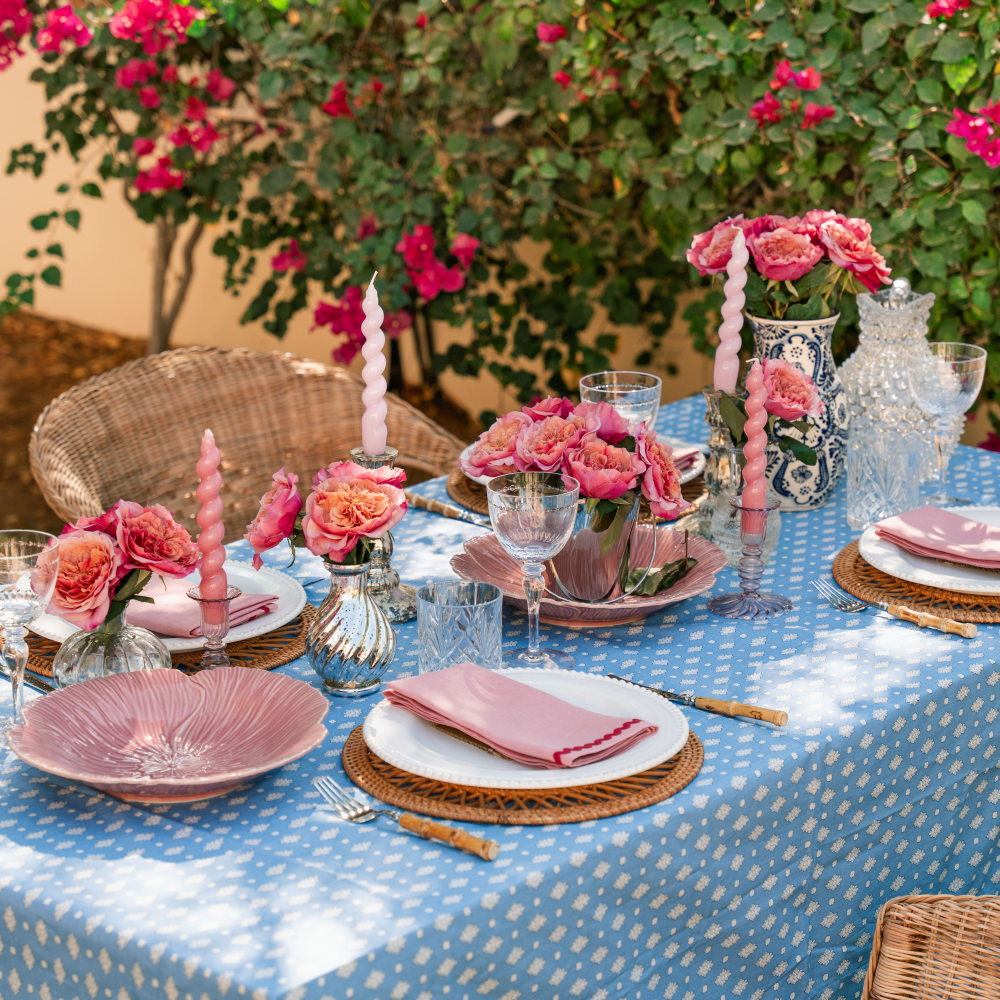 Elegant outdoor table setting with pink floral arrangements and candles on a blue polka dot tablecloth.