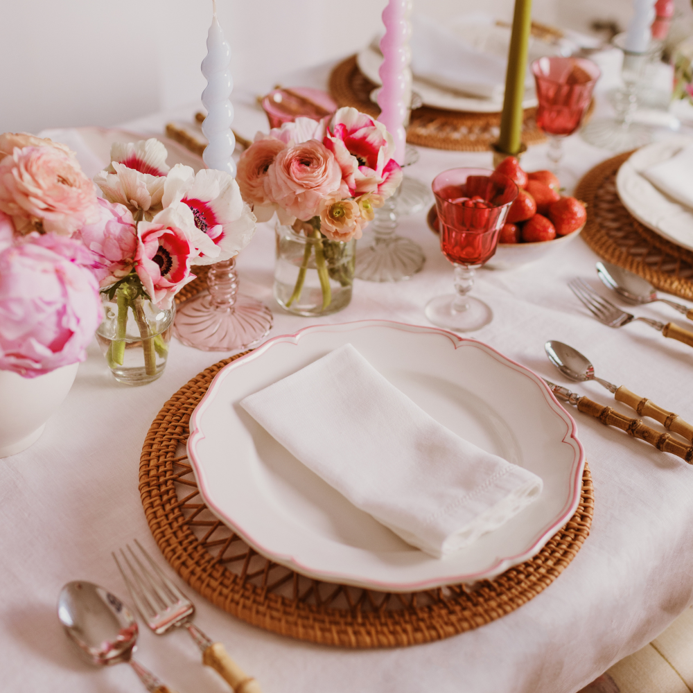 Elegant table setting with pink flowers, white plates, and cutlery on a white tablecloth.