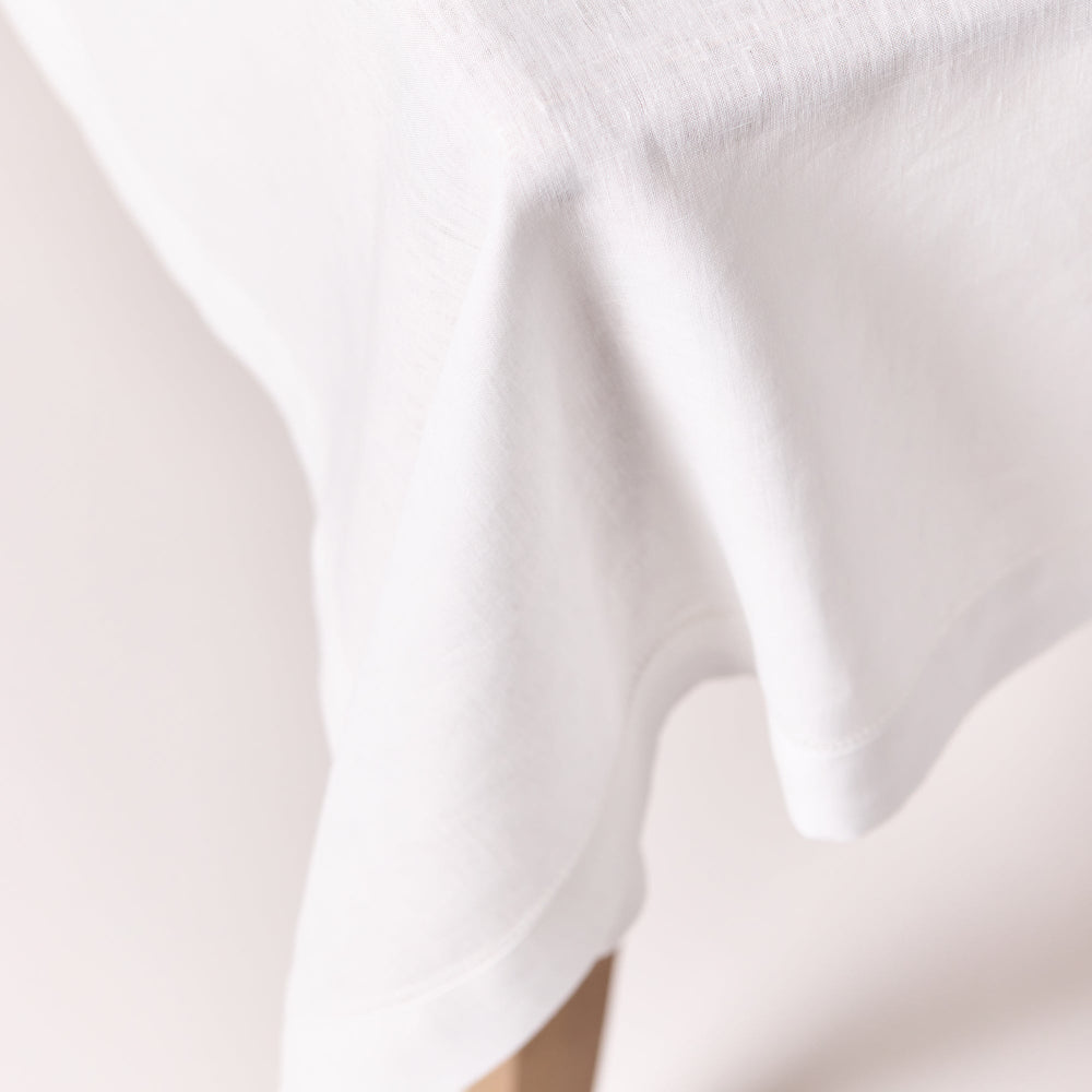 Close-up of white linen tablecloth with hemstitched edges with folds draped over a dining table.