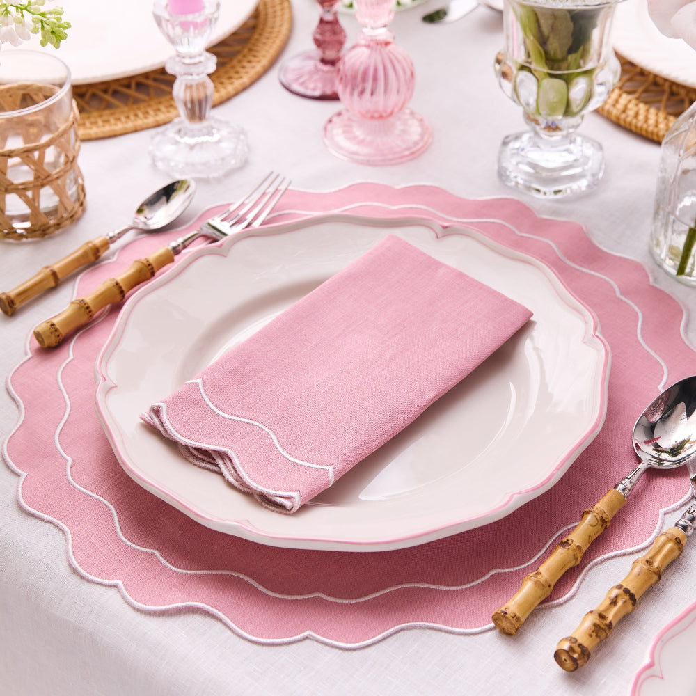 Table setting with pink plates, napkins, and cutlery on a white tablecloth.