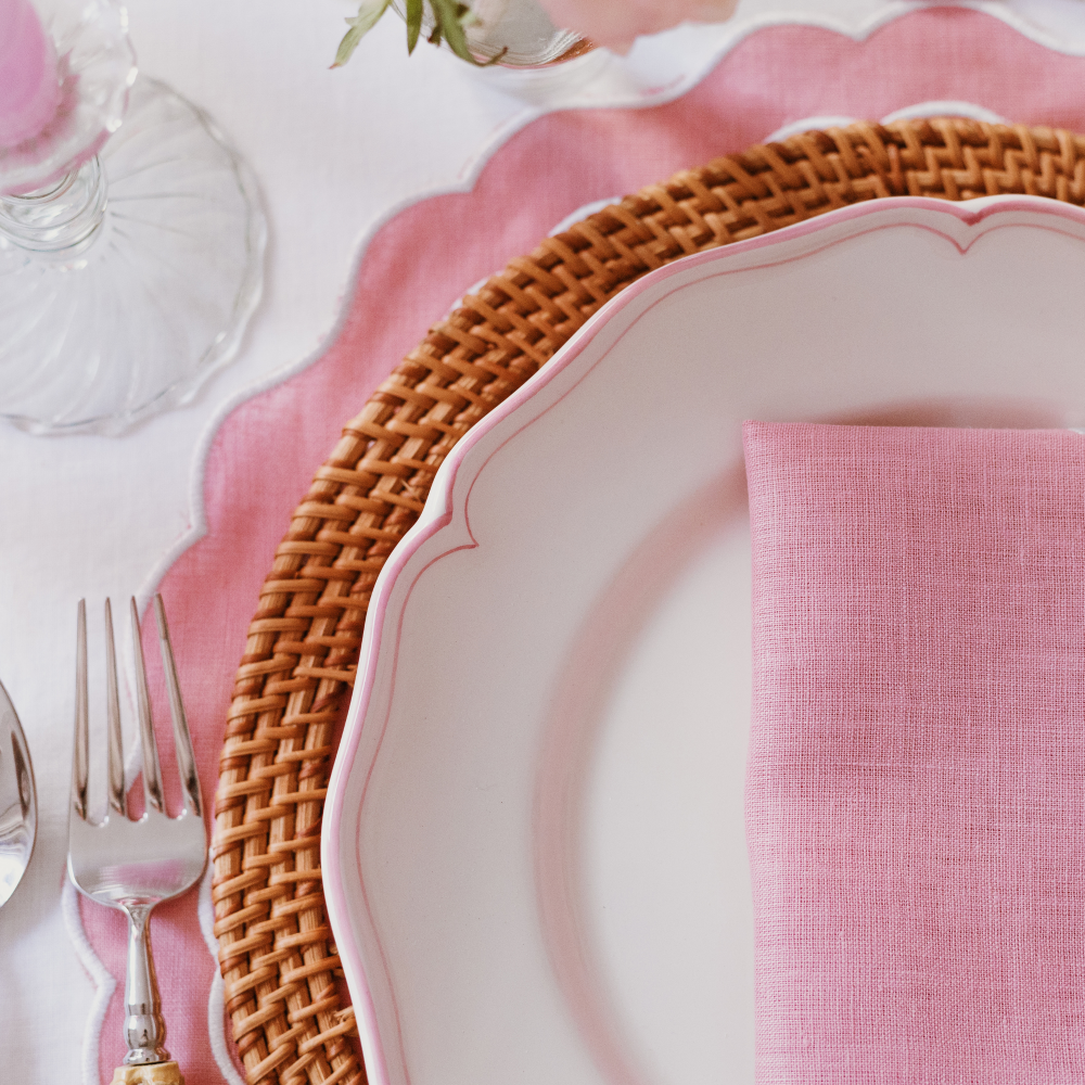 Table setting with pink scalloped placemat, napkin, and wicker charger.