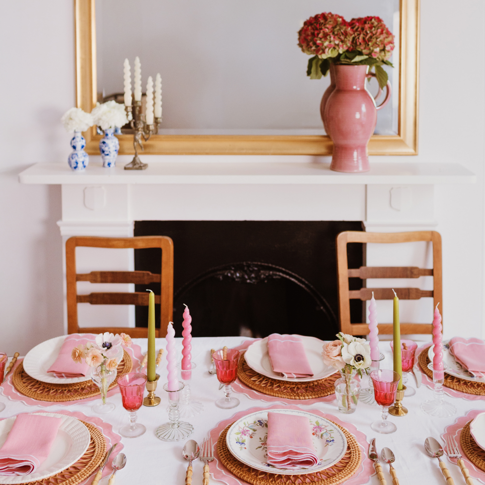 Dining table set with pink and gold accents in a room with a fireplace and mirror.