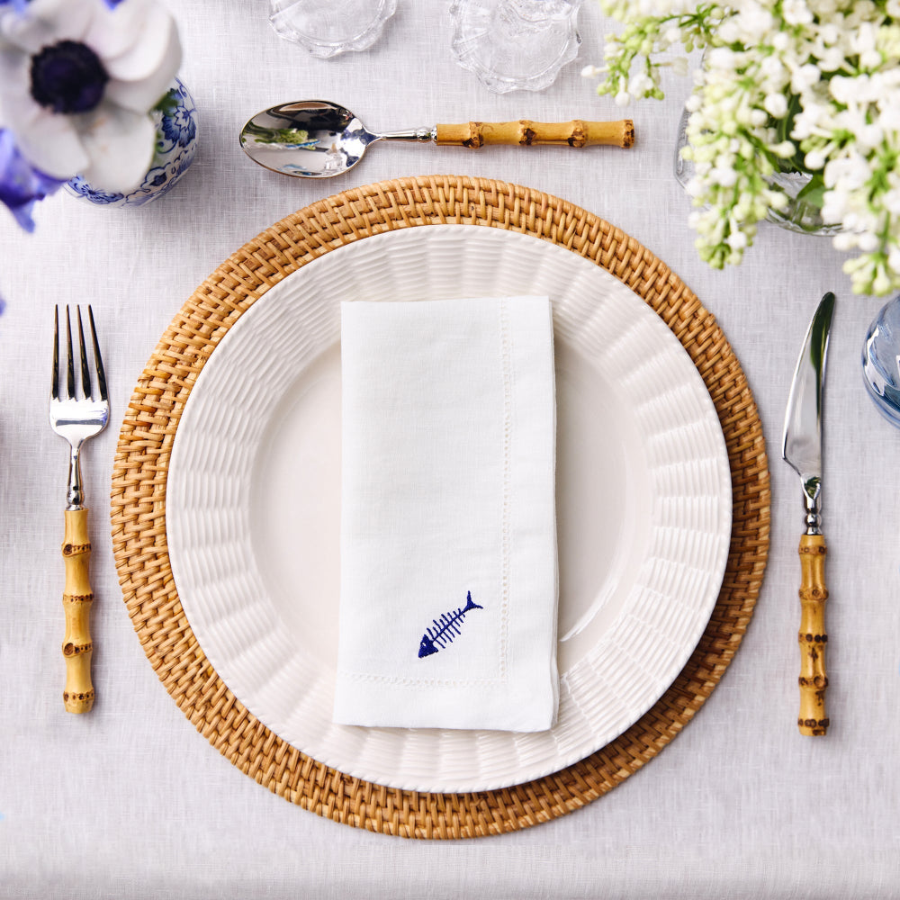 Table setting with white plates, wicker chargers, and decorative napkins on a light grey surface.