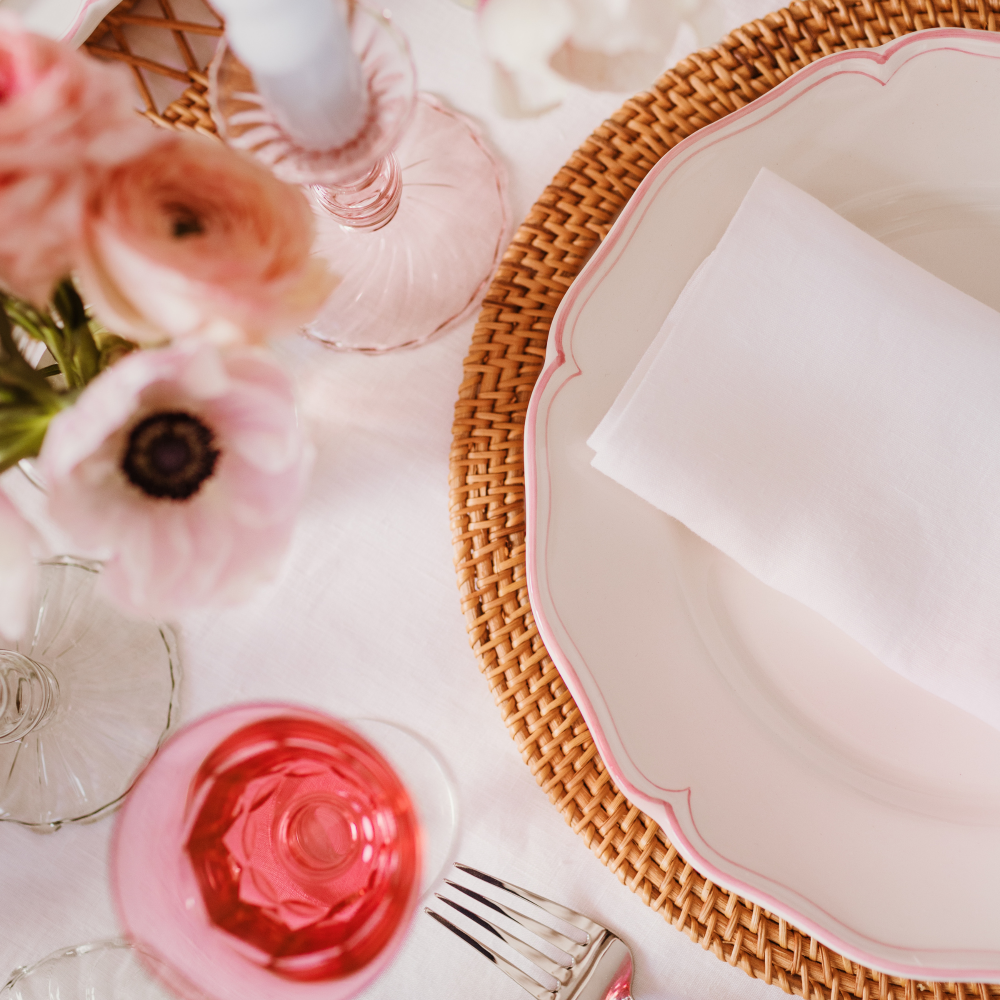 Table setting with pink floral glasses, a woven placemat, and white napkin.