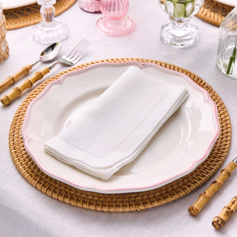 Dining table setting with a white plate, folded linen hemstitched napkin, and wicker placemat.