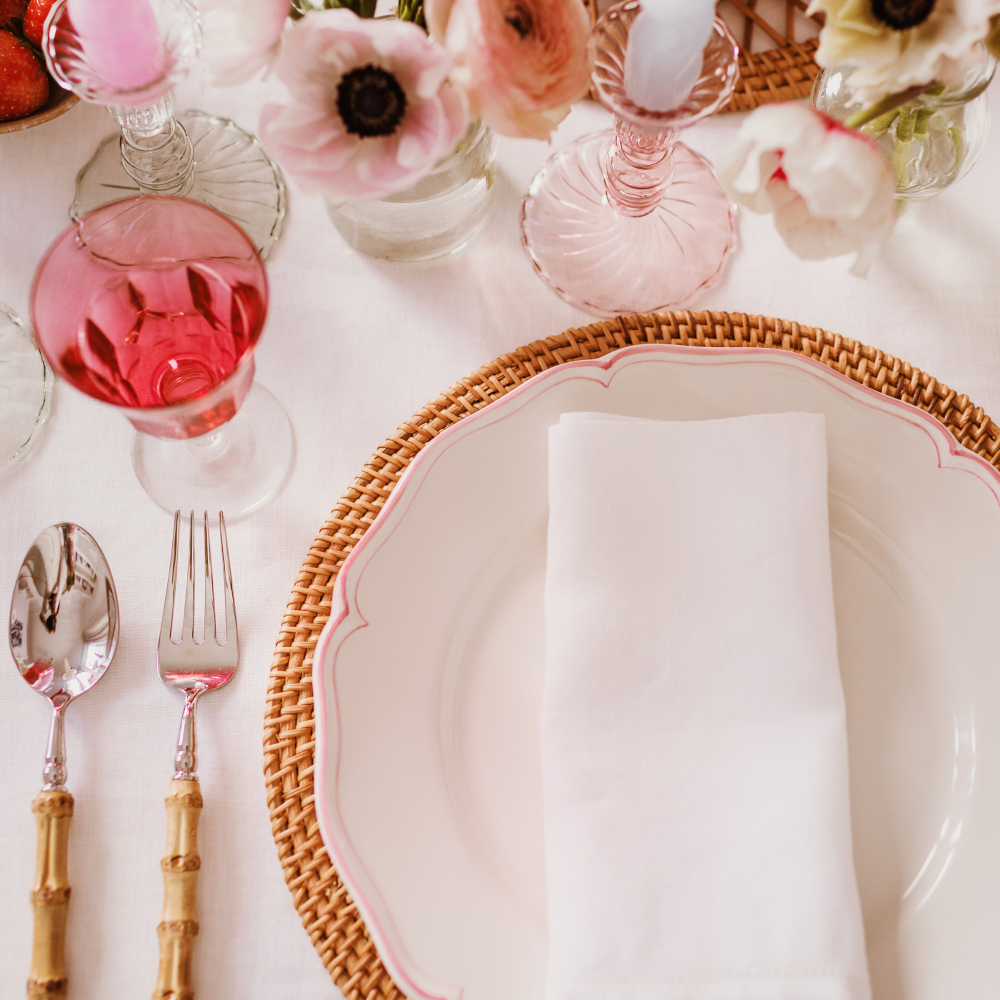 Elegant table setting with a woven charger, white plate, white linen napkin and decorative glasses.