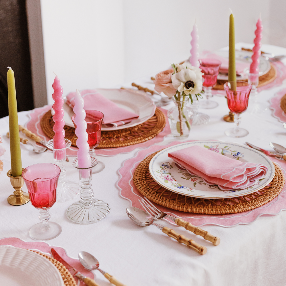 Elegant table setting with pink candles, glasses, and floral decorations on a white tablecloth.