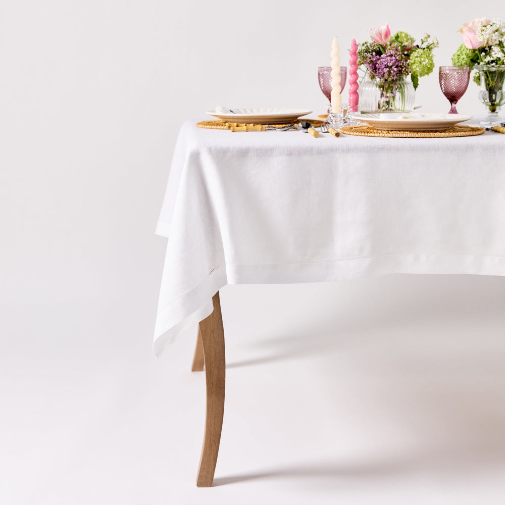 Elegant table setting with white tablecloth, gold plates, pink candles, and floral arrangements on a plain background.