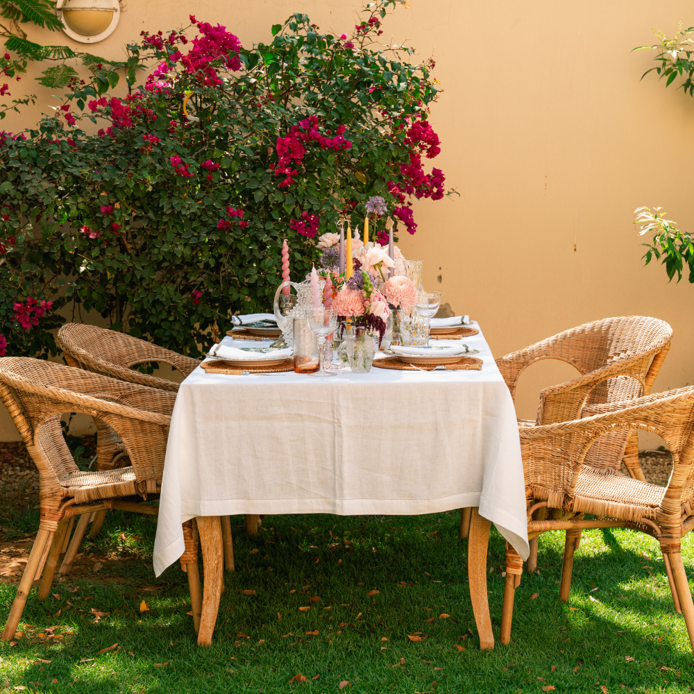Dining table set with flowers and plates outdoors against a beige wall with greenery.