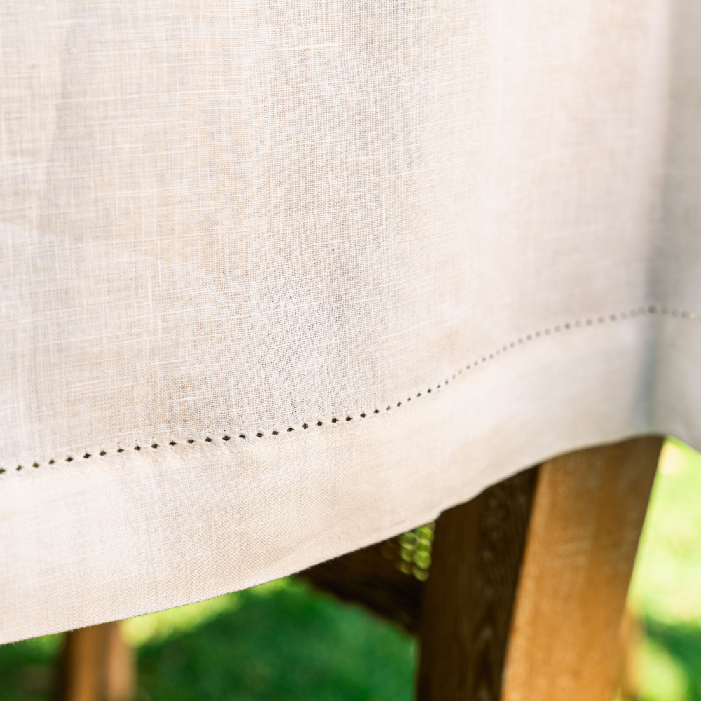 Close-up of a white linen tablecloth fabric with a wooden chair and blurred greenery in the background