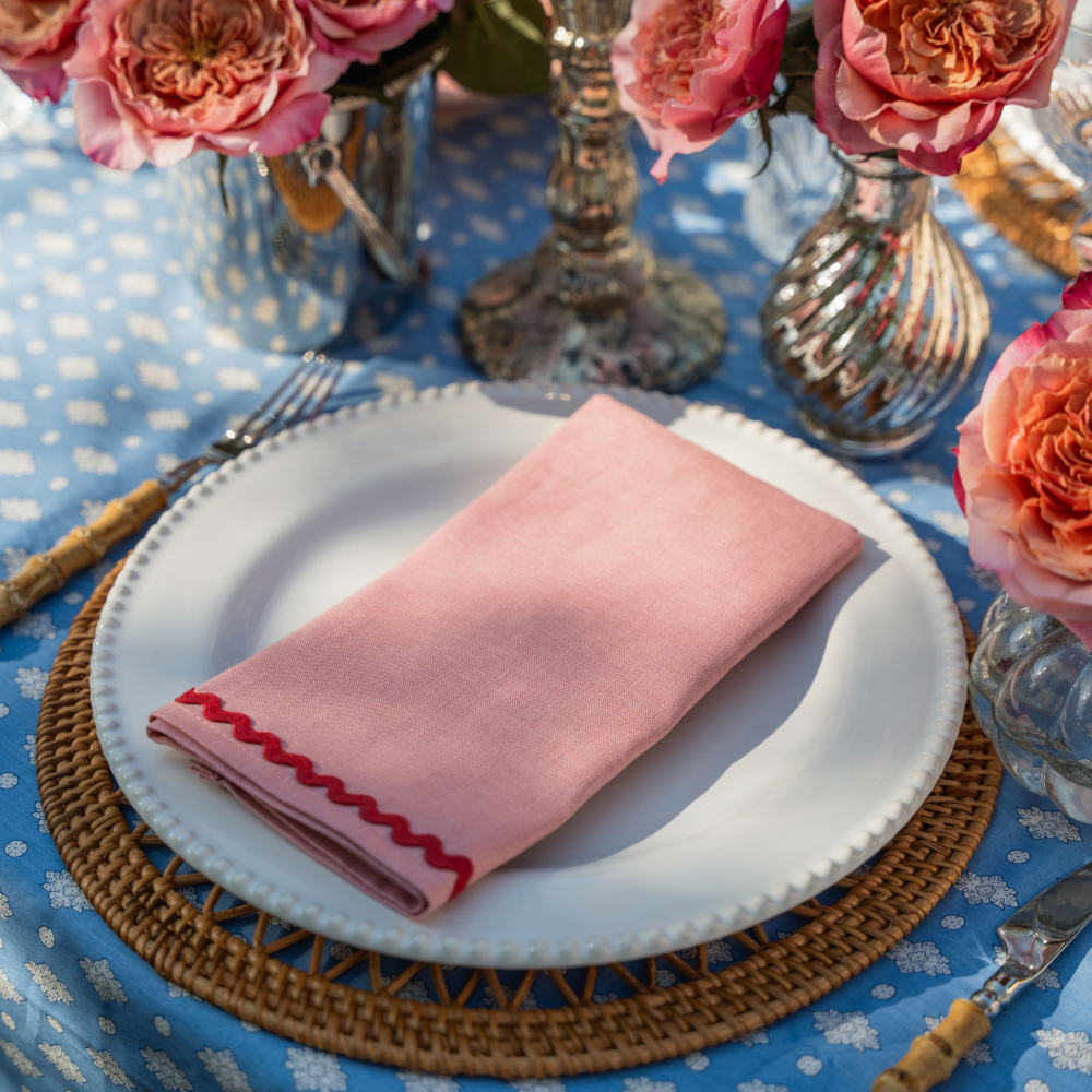 Table setting with pink napkin, white plate, and floral decorations on a blue tablecloth.
