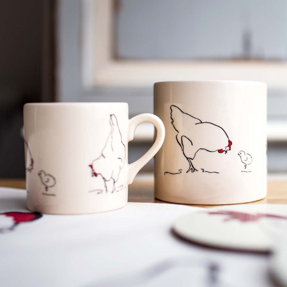 Two ceramic mugs with chicken illustrations on a surface.