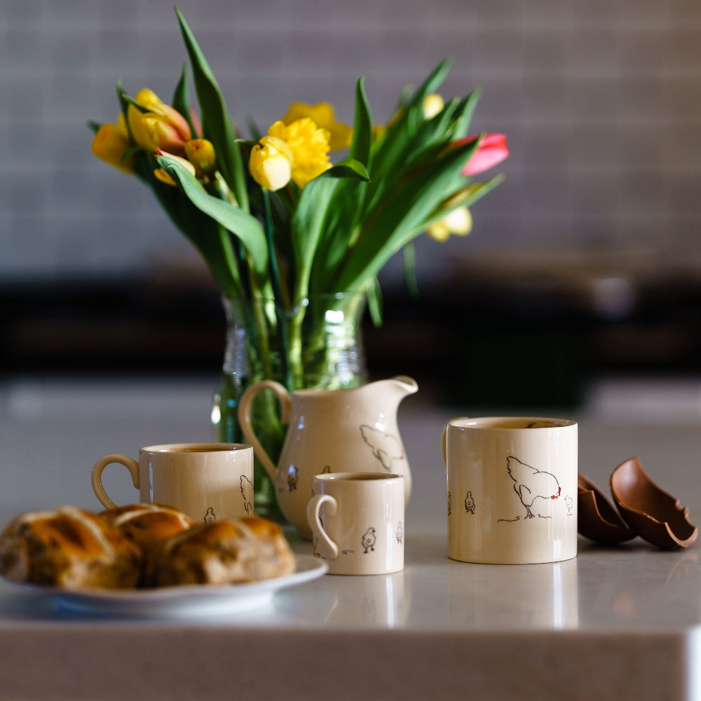 Ceramic mugs, a pitcher, and a vase with flowers on a table.
