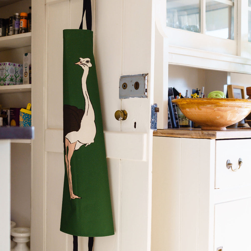 Green apron with a bird design hanging on a kitchen cabinet.